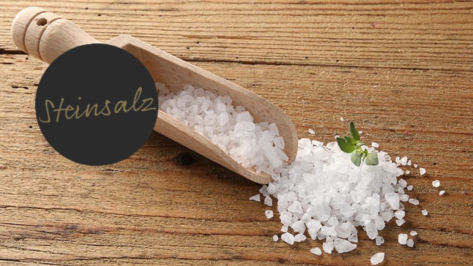 Präsentation eines Holzlöffels mit Steinsalz auf einem Holzbrett, das eine einfache, aber ansprechende Küchenszene schafft.