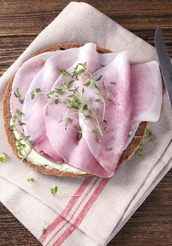 Kochschinken auf einer Scheibe Brot, appetitlich angerichtet, mit frischen Kräutern garniert.