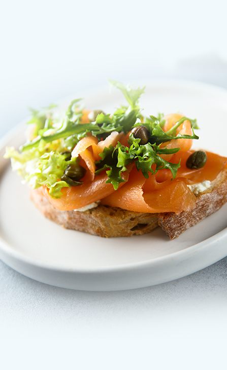 Lachsbrötchen auf einem weißen Teller, dekoriert mit grünem Salat.