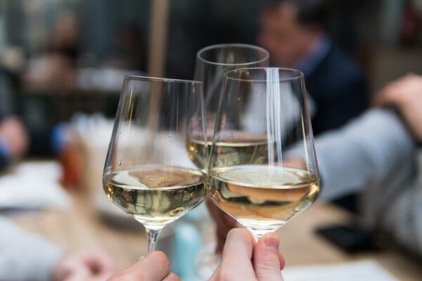 Drei Weingläser stoßen aneinander, gefüllt mit Wein, vor einem unscharfen Hintergrund. 