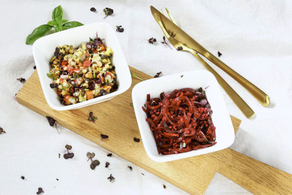 Linsensalat und Rote-Bete-Salat auf einem Holzbrett angerichtet, umgeben von frischen Kräutern und Gewürzen.  