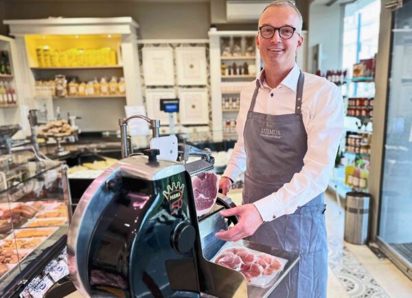Stephan Helmus, Metzgermeister, lächelt in die Kamera, während er eine Parma Aufschnittmaschine bedient.