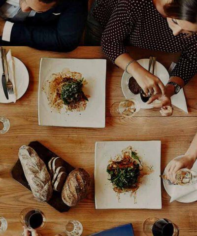 Gedeckter Tisch aus der Vogelperspektive, umgeben von Personen, die sich unterhalten und essen. 
