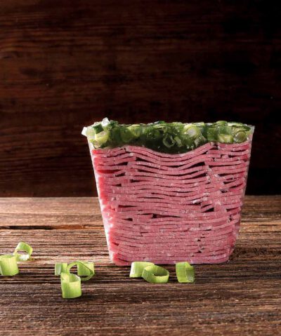 Produktaufnahme von Sülze mit Frühlingszwiebeln auf einem Holzbrett, ansprechend angerichtet. 