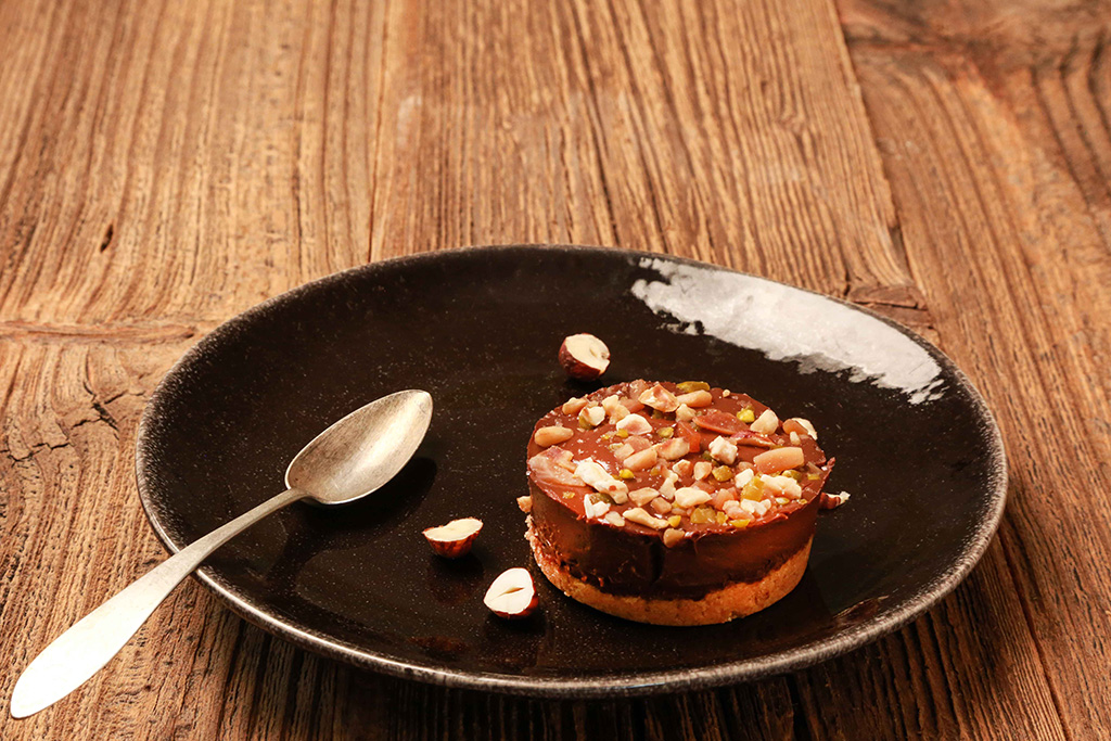 Patisserie Sable-Gianduja auf einem schwarzen Teller, verziert mit Mandelsplittern.