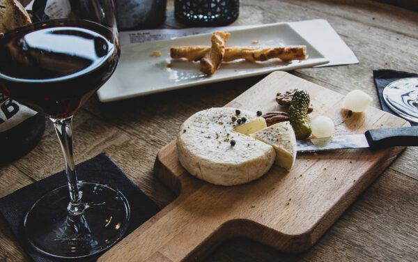 Käse auf einem Holzbrett, platziert auf einem Tisch neben einem Weinglas. 