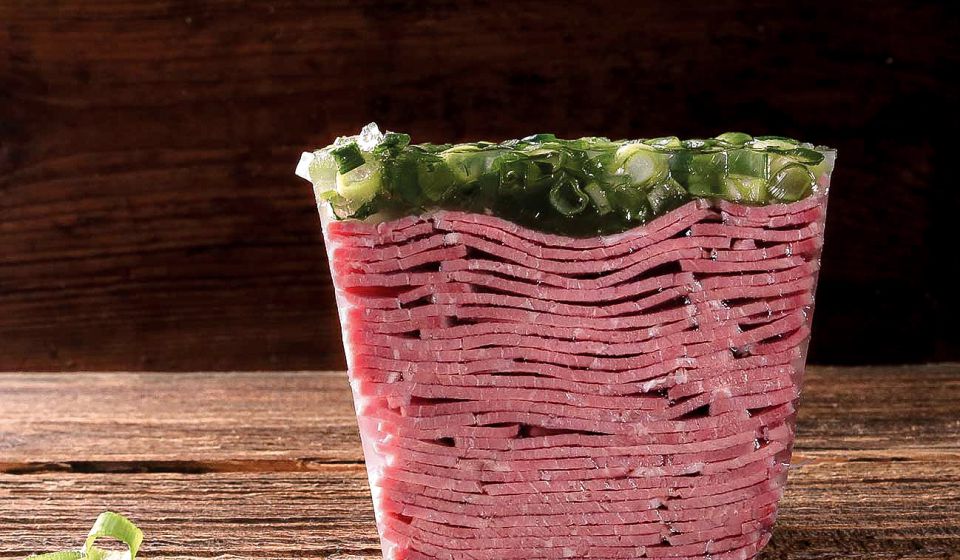 Holzbrett mit hausgemachter Sülze, kunstvoll garniert mit frischen Kräutern.